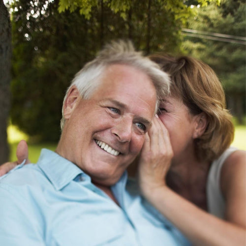 Older woman whispering in an older man's ear, smiling