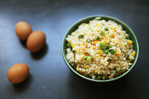 Bowl of egg fried rice next to three eggs