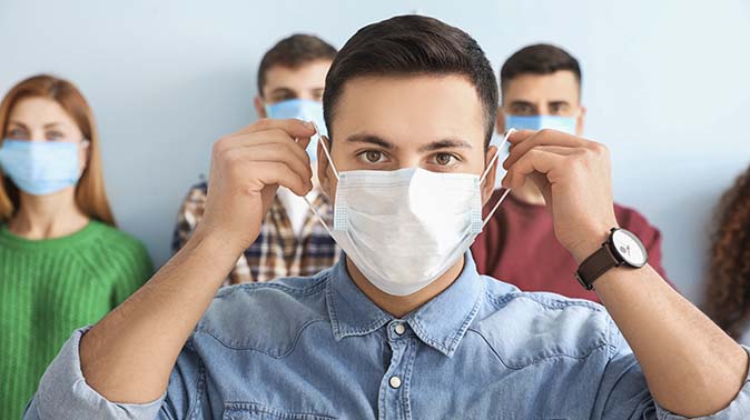 A man putting on a mask, with a group of people behind him also wearing masks