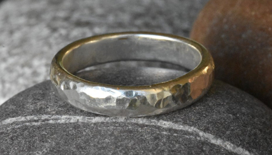 Chunky Eco Silver Ring with Dimple Texture, pictured on a dark grey pebble with light grey and light brown pebbles in the background. 