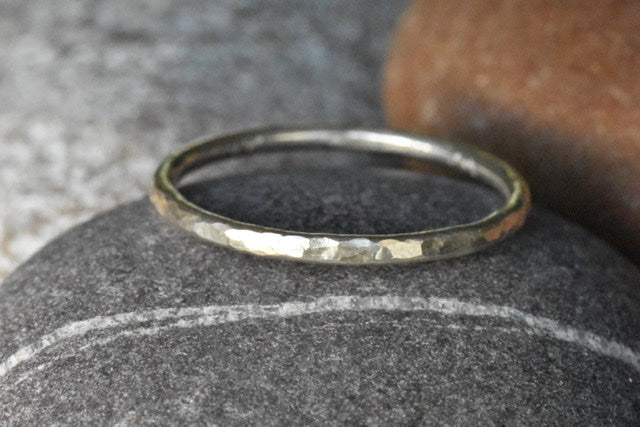 Eco Silver Ring with a Dimple Texture, pictured on a dark grey pebble with light grey and light brown pebbles in the background.