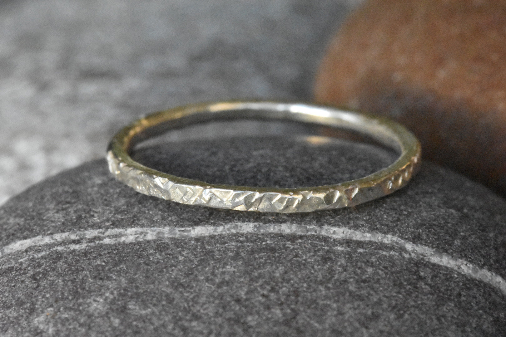 Eco Silver Stacking Ring with Chequer Texture on dark grey pebble with light grey and light brown pebbles in the background. 