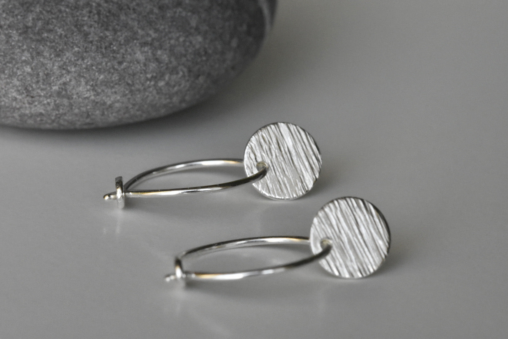 Eco Silver Hoop Earrings with a line textured disc on each one, front view.