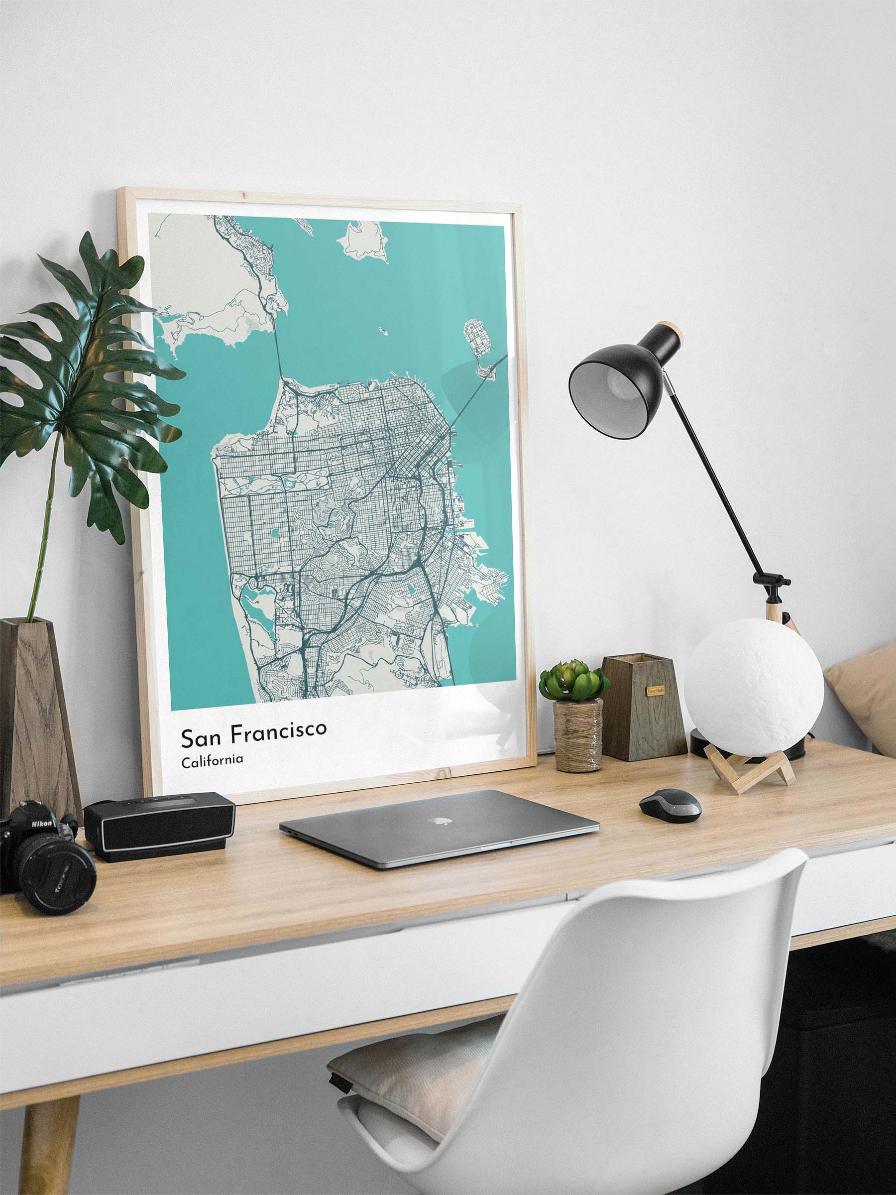 Famed map art print of San Francisco, California, on a work desk with a laptop and a lamp.