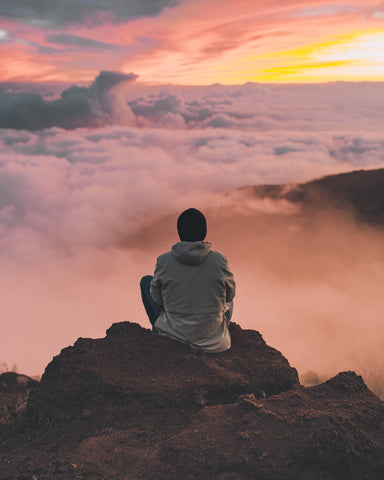 Man looking outward over the clouds on top of a hill