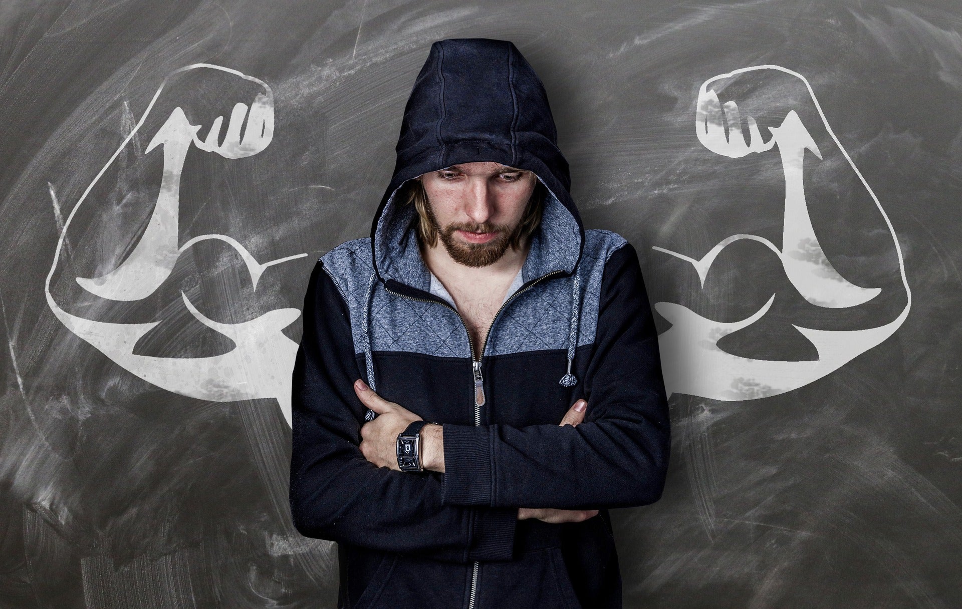 Man sitting in front of blackboard that has a picture of muscly arms