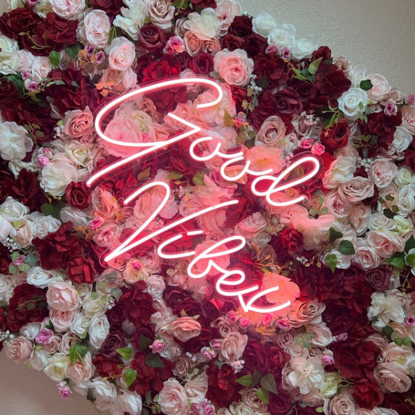 Customer's pink Good Vibes neon sign on a floral wall.