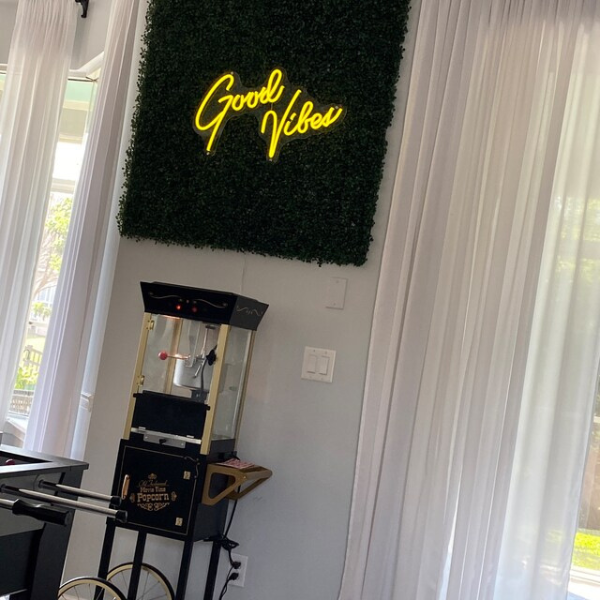 Customer's golden yellow good vibes neon sign installed onto greenery and hanging above their popcorn machine in their living room.