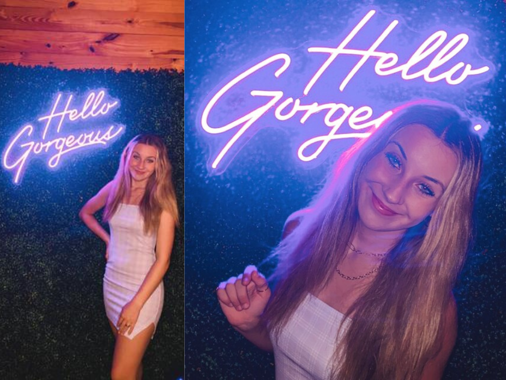 Customer posing infront of their purple Hello Gorgeous neon sign in a purple and white checkered dress.