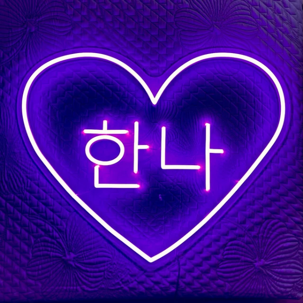 Hanna in Korean letters inside a heart neon sign. Sign is in the color purple. Sign is installed onto wall.