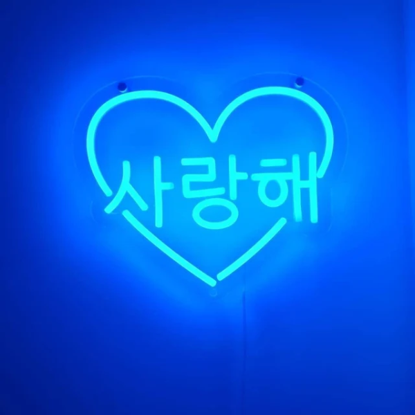 Love you in Korean letters inside a heart neon sign. Neon sign is in the color Electric Blue. Neon sign is installed onto a wall.