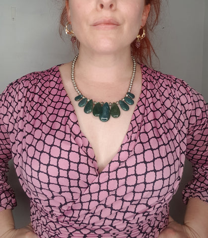 A woman in a V neck dress wearing a green agate necklace just below the clavicle