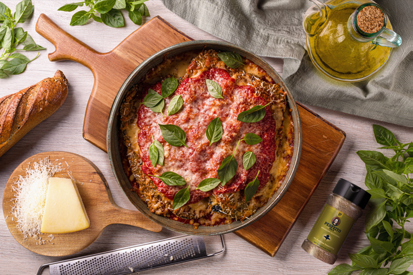 Eggplant Parmesan with crispy layers, marinara, melted cheeses, and basil on a rustic table, surrounded by fresh ingredients.