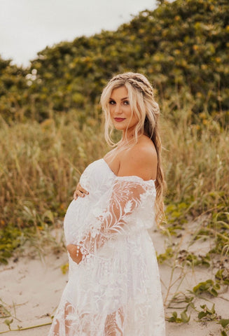 Pregnant lady wearing a white off-shoulder lace gown in beach setting for her maternity shoot