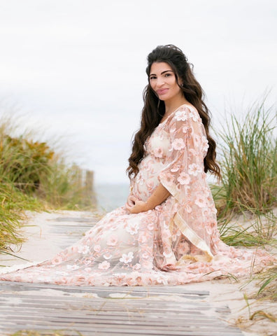 Lady wearing floral kaftan dress poses on the beach for her pregnancy photos