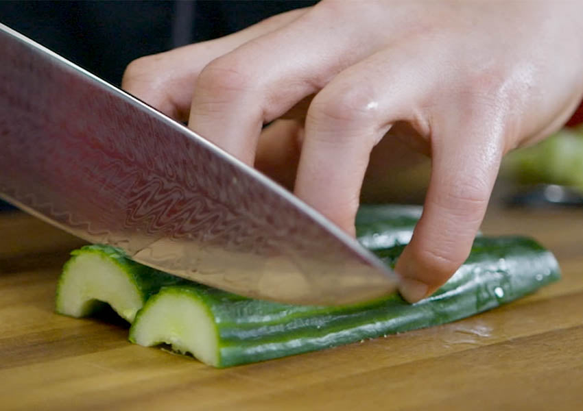 hand holding cucumbers in place using the claw grip