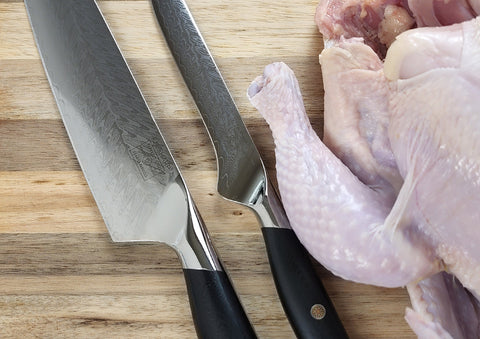 Using kitchen knife to cut raw chicken leg away from flesh