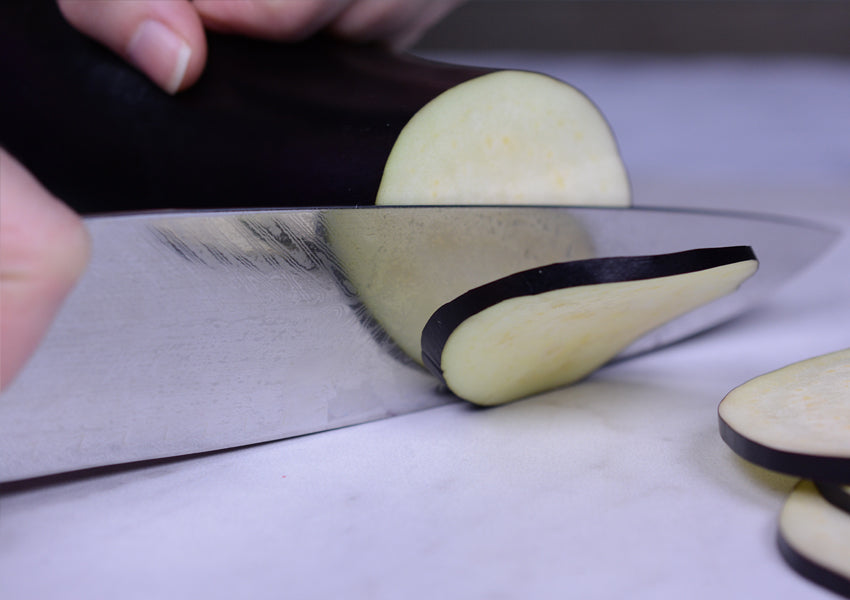 Slicing eggplant with chef's knife on ceramic cutting board