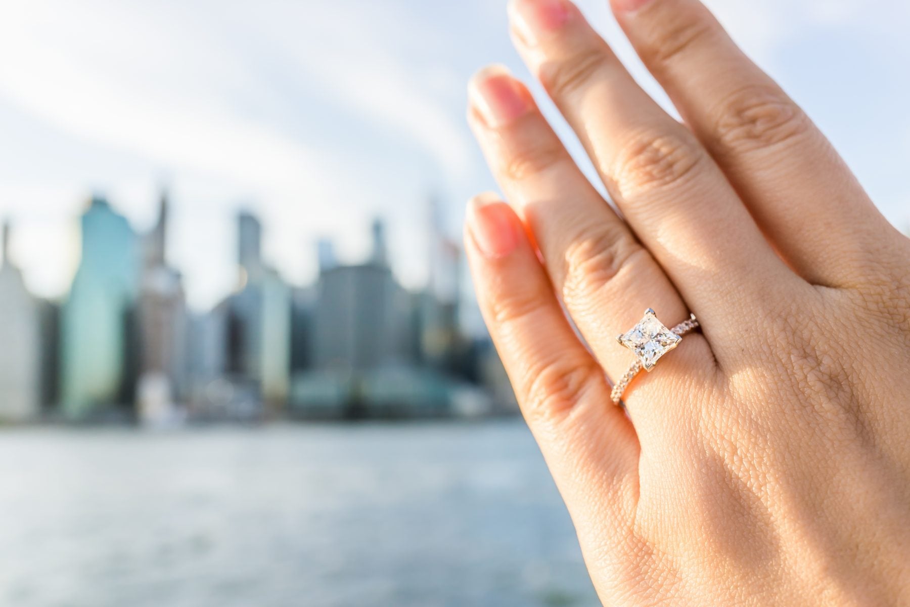 woman wearing princess cut diamond ring skyline city background