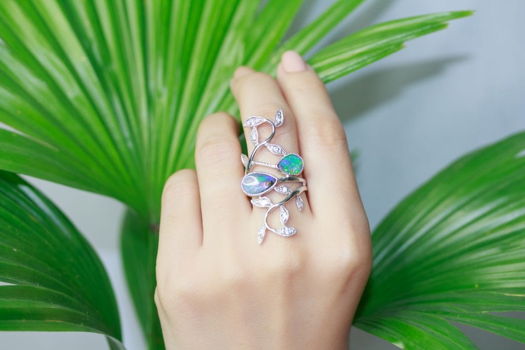 woman's hand with opal ring in front of green leafs