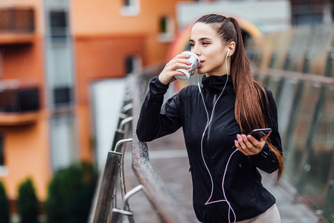 A woman walking with earphones and drinking from a paper cup