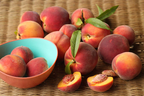 Fresh peaches spilling out of a bowl on a table.