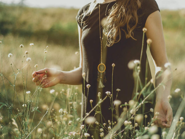A spiritual woman walks through a meadow touching the long stemmed flowers in the sun