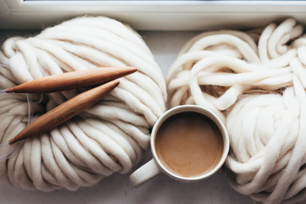 Beige wool ball with wooden knitting needles and a warm mug of tea