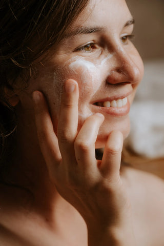 A smiling girl puts canvas cream cleanser on her face