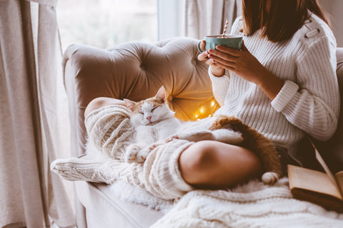 Hygge vibes with a boho girl cosy on the sofa with a cup of cocoa and a cat snuggled up