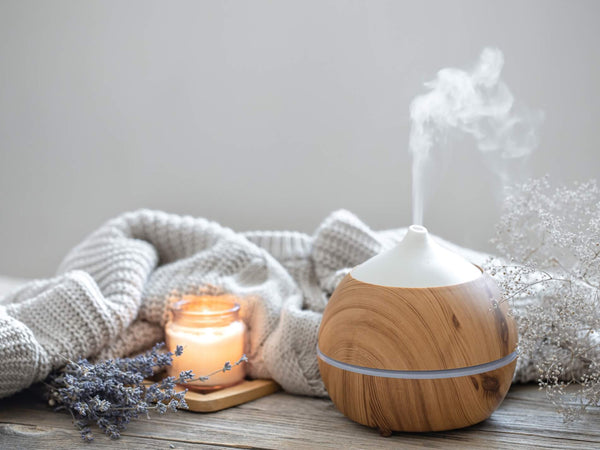 A hygge autumn scene with aromatherapy diffuser, candle and cosy blanket