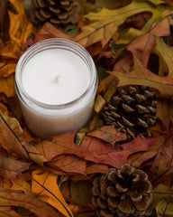 White candles on a bed of orange and brown autumn leaves with a couple of pine cones