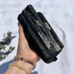 A large black tourmaline crystal log held to camera in the sun