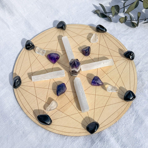 A crystal grid board with amethyst, tourmaline and selenite laid in a geometric pattern for protection