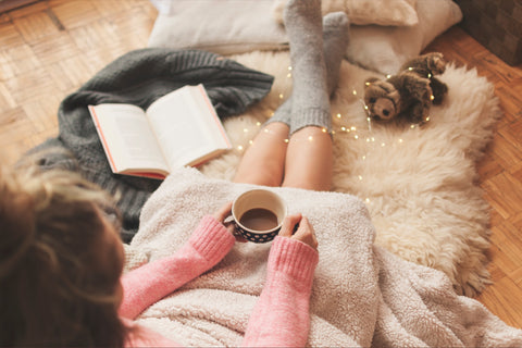 Girl sits in a cosy pile of sheepskin rugs with a book and mug of cocoa