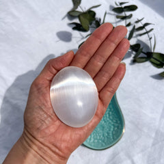 A glimmering white selenite crystal palm stone held to camera