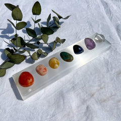 Seven rainbow coloured chakra crystals on a white selenite crystal bar