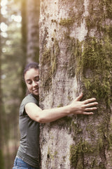A woman with a smile on her face hugging the trunk of an old oak tree