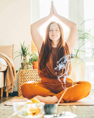 A young red headed woman sits in a yoga pose in front of crystals and incense