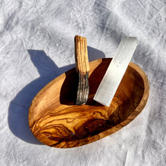 An olive wood bowl with a smoking Palo Santo wood and selenite crystal wand