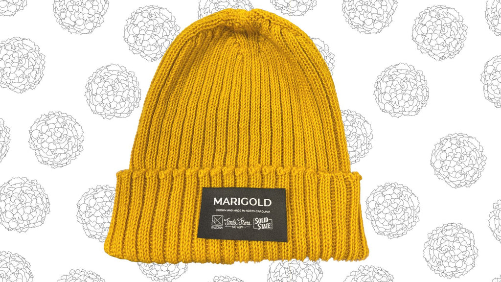 a golden-yellow wool beanie hat on a backgroud of illustrated marigold flowers