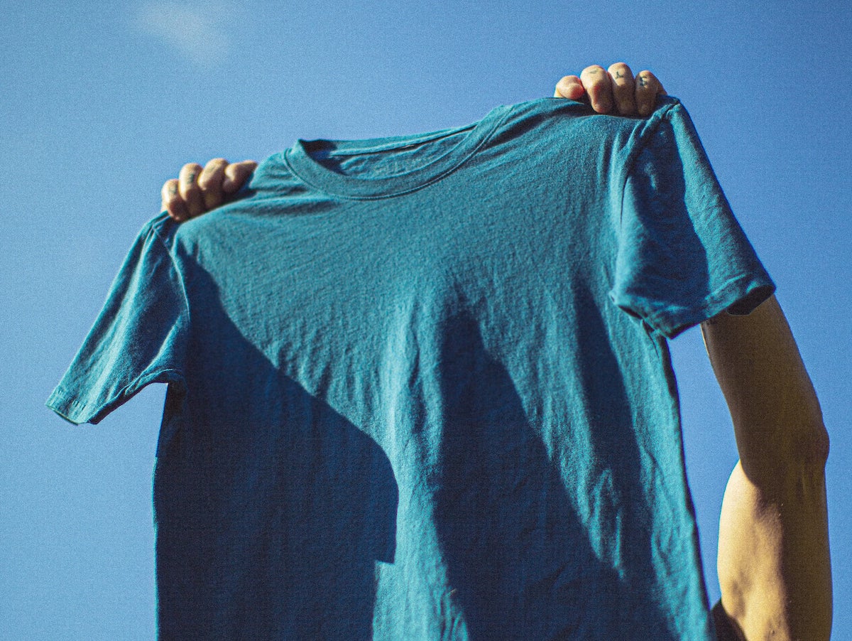 a blue t-shirt being held up above someone's head on the background of a blue sky