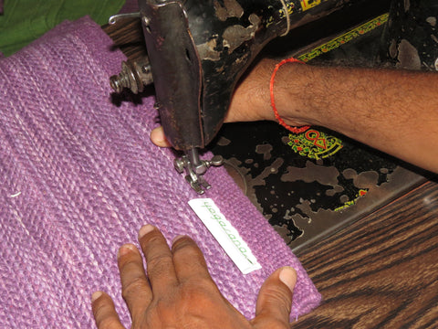 Closeup of weaver sewing Yogasana label on an organic cotton purple yoga rug