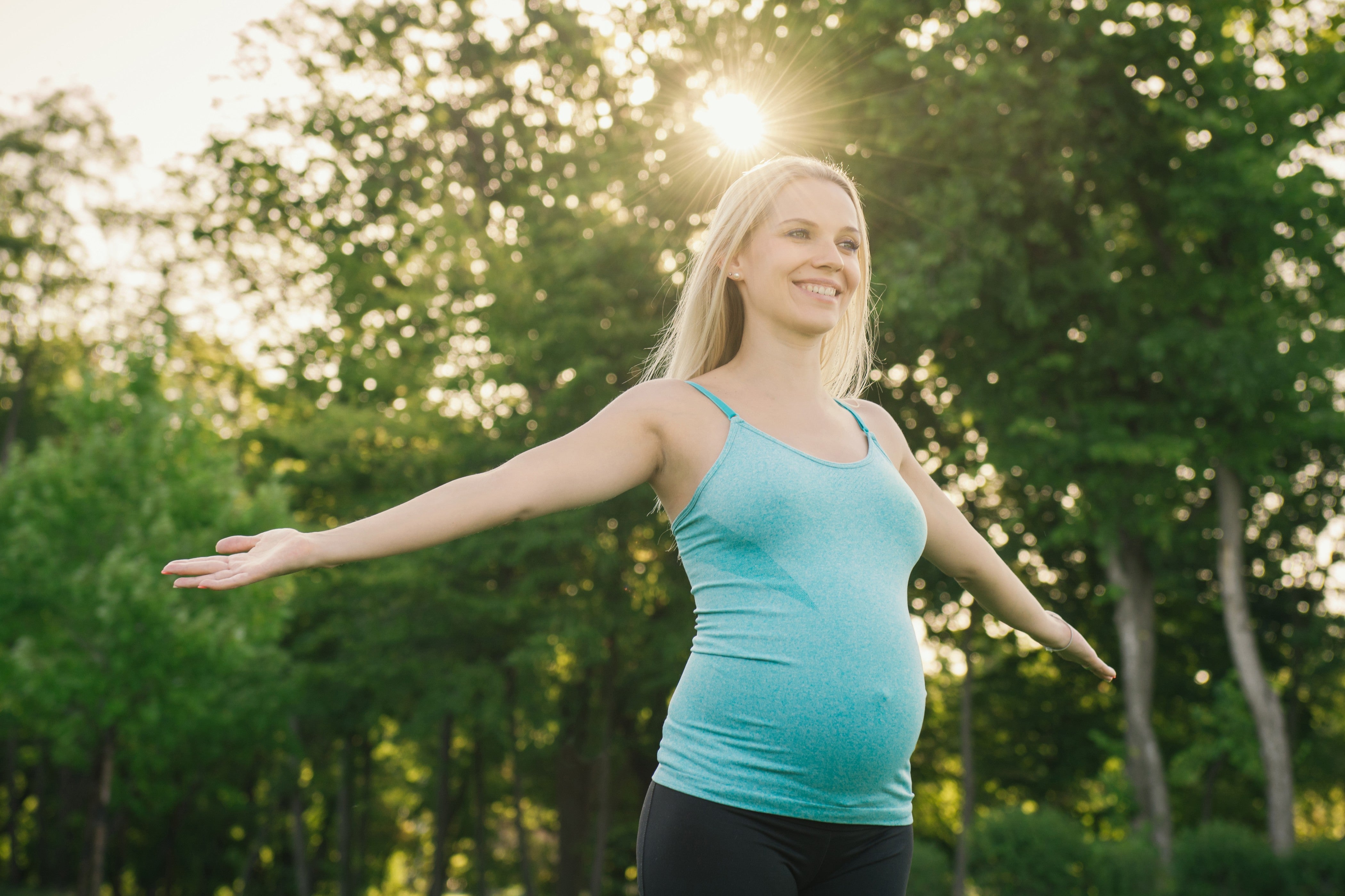 Pregnant woman out in nature with the sun shining behind her
