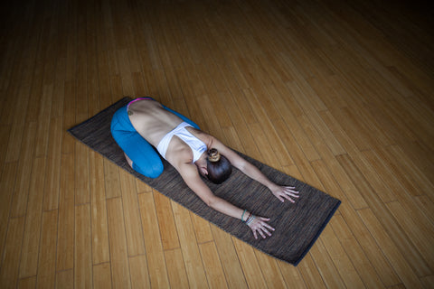 Yogi in child's pose with face on brown cotton yoga mat.