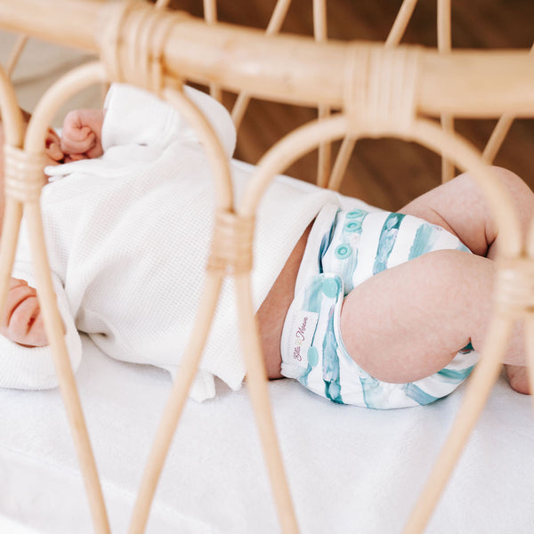 Newborn baby laying in a rattan bassinet wearing a cloth nappy