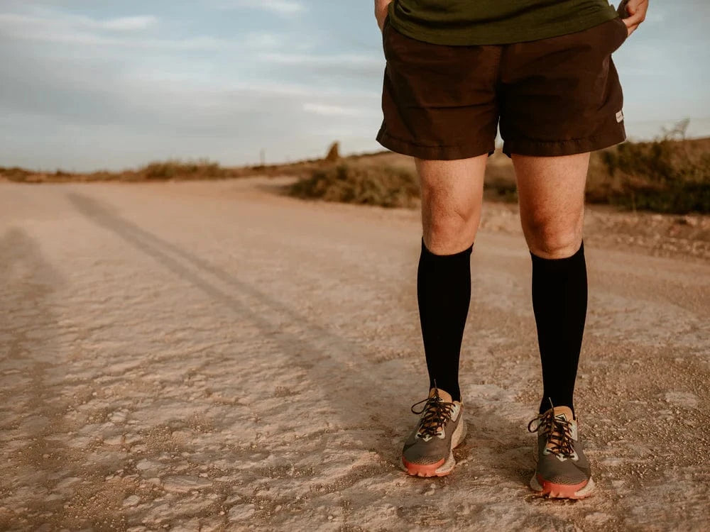 Person standing on a dirt path wearing running shoes, black socks, and shorts.