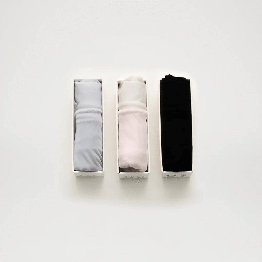 Three rolled-up shirts in white boxes: light gray, pale pink, and black.