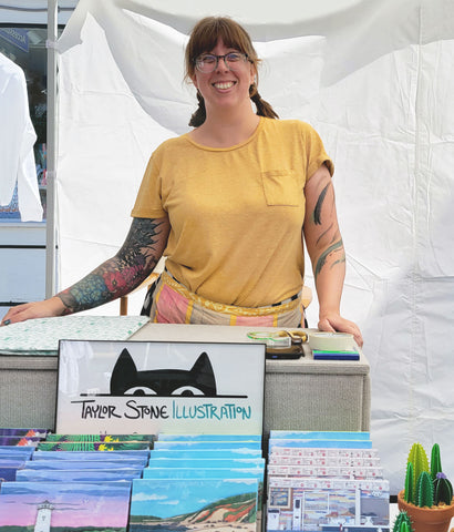 Woman standing behind a picture of a cat at an open air market.