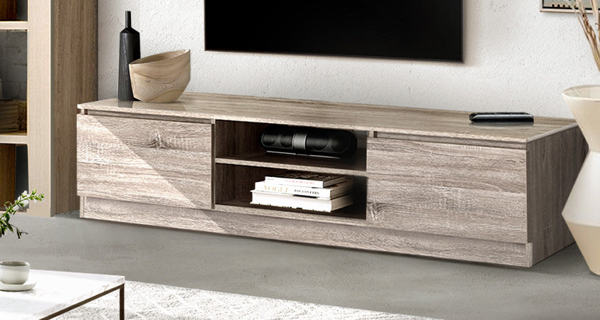 The Artiss Jason entertainment unit is featured in a living room with a concrete floor and white rug. The centre shelves are holding a stack of books and a soundbar, while on top are a remote and two decorative vases. Above can be seen a wall mounted plasma TV.